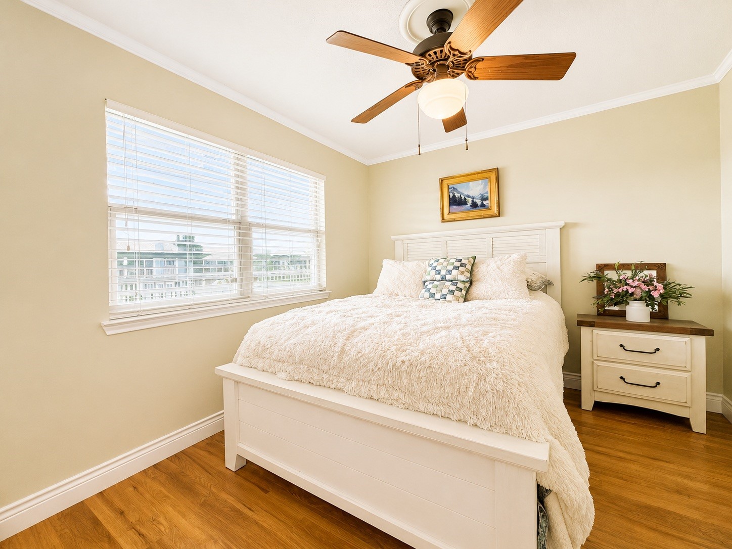 135 Sand Shoals Road Freeport, TX 77541 - Photo 17 of 20 Bright and cozy bedroom with a large window, wooden floors, and a ceiling fan. It features a comfortable bed, soft bedding, and a bedside table with flowers, creating a welcoming atmosphere.