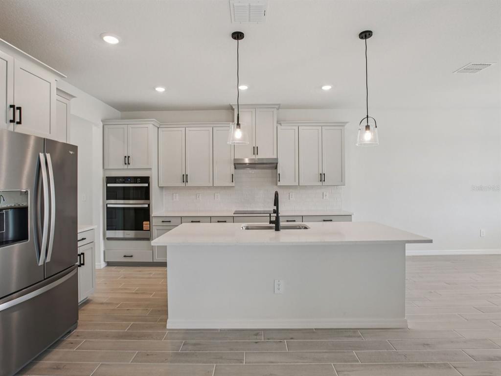 10821 Heirloom Farms Run Parrish, FL 34221 - Photo 2 of 13 a large kitchen with stainless steel appliances kitchen island granite countertop a refrigerator a oven a sink and a granite counter tops