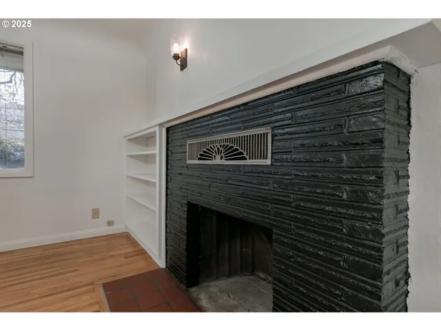 a view of an empty room with wooden floor and a fireplace