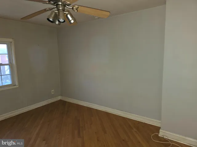 an empty room with a chandelier fan and wooden floor