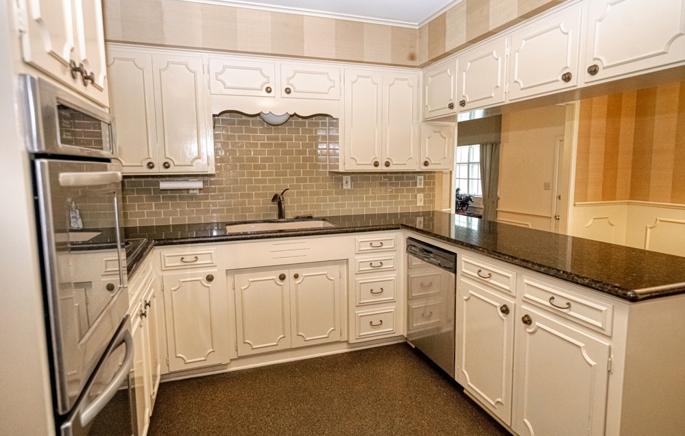 301 Cedar Circle Brenham, TX 77833 - Photo 8 of 20 Kitchen with a peninsula, dark stone countertops, appliances with stainless steel finishes, backsplash, and wallpapered walls