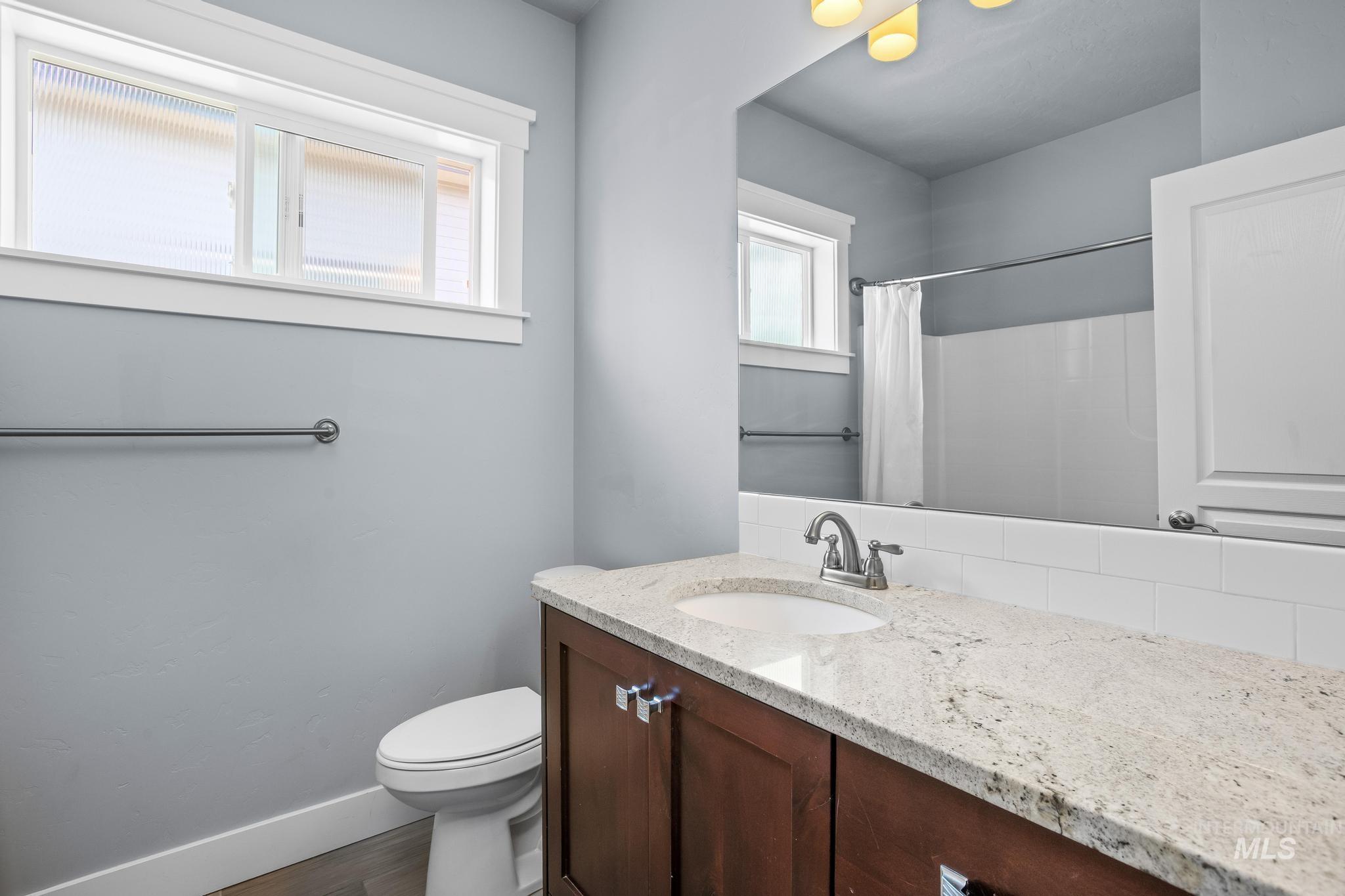 2681 East Rhyolite Court Nampa, ID 83686 - Photo 35 of 48 Bathroom featuring a white vanity with a light-colored countertop and a wood-finish base, a white subway tile backsplash, and a window with white trim