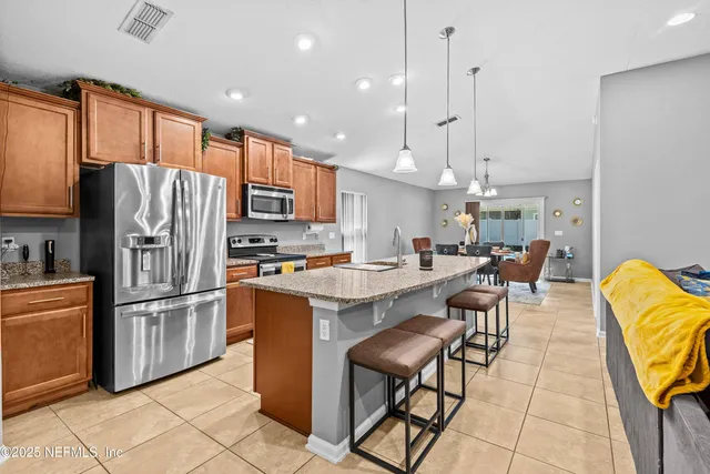 a kitchen with stainless steel appliances granite countertop a refrigerator a sink a stove a dining table and chairs with wooden floor