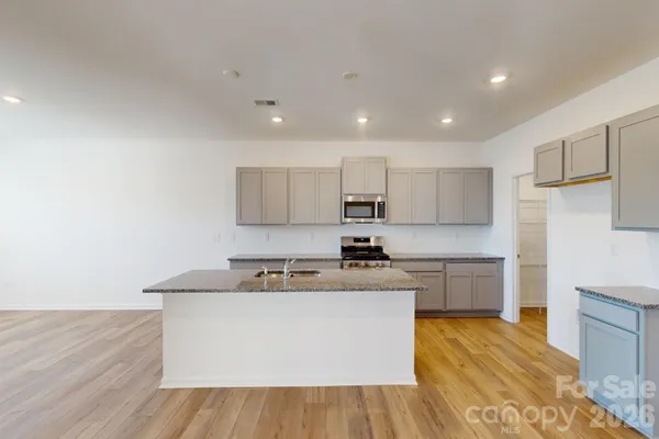 a large kitchen with stainless steel appliances granite countertop a stove a sink a refrigerator and white cabinets with wooden floor