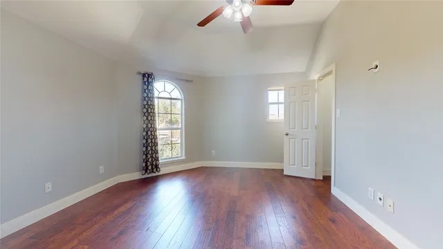 an empty room with wooden floor chandelier fan and windows