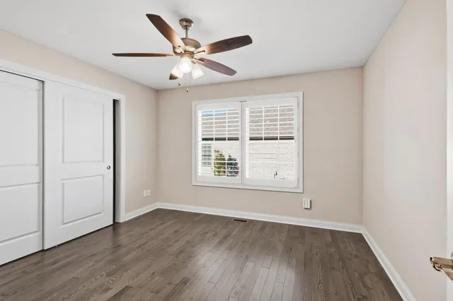 an empty room with wooden floor chandelier fan and windows