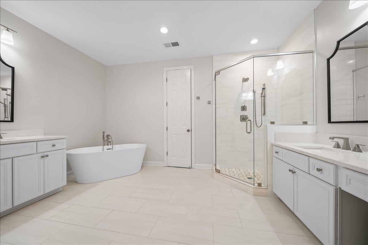 1876 Liles Lane Collierville, TN 38017 - Photo 13 of 36 Freestanding soaking tub with floor-mounted faucet, frameless glass shower enclosure, dual vanity sinks with white cabinetry, and large format tile flooring