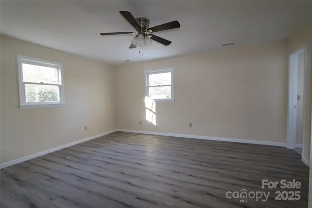 an empty room with wooden floor a ceiling fan and windows
