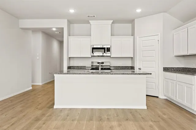 a large kitchen with stainless steel appliances granite countertop a stove a sink and white cabinets