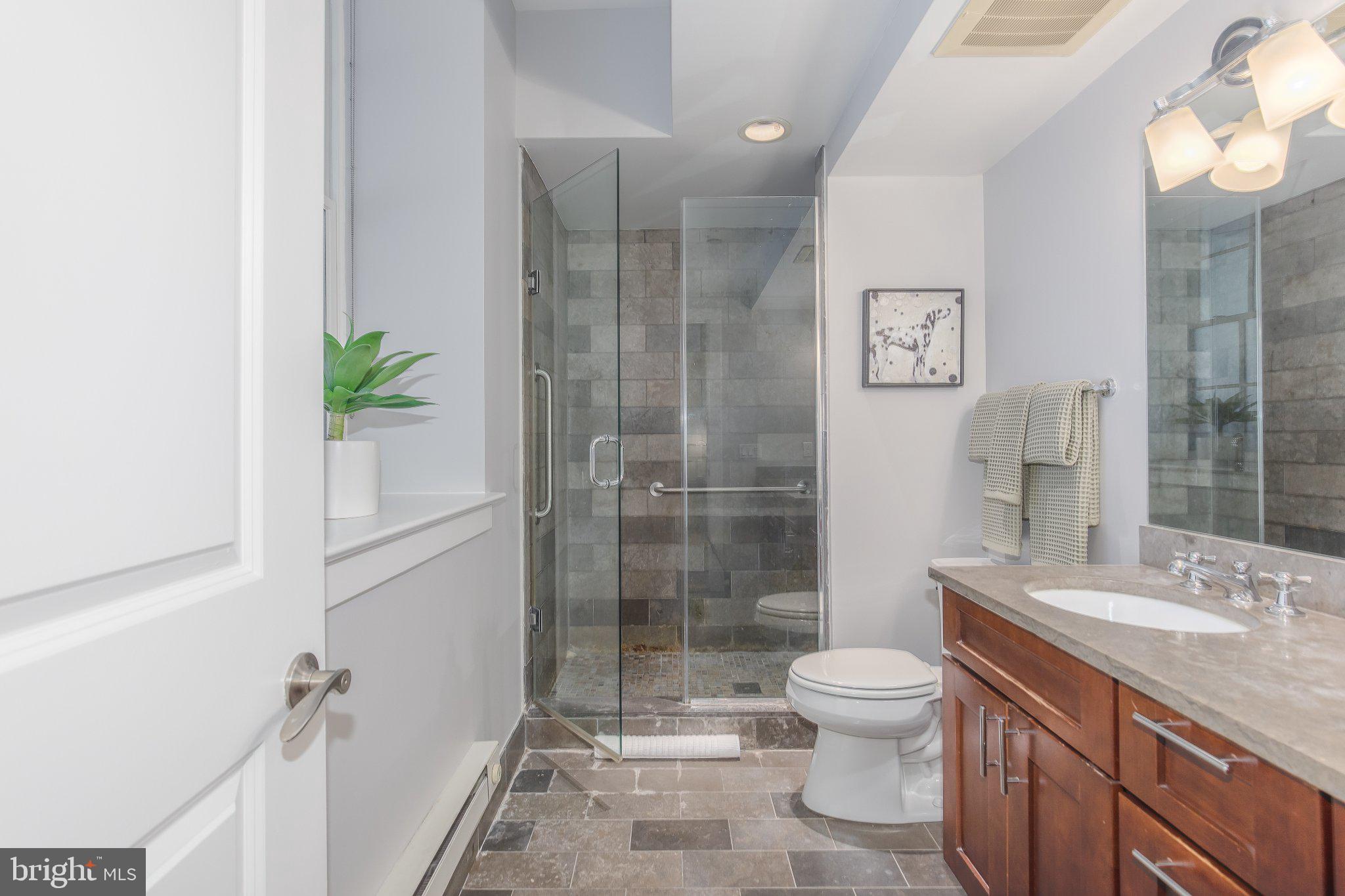 215 I Street Northeast, Unit 105 Washington, DC 20002 - Photo 32 of 41 a bathroom with a granite countertop sink toilet a large mirror a glass door shower and a bathroom