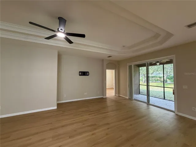 an empty room with wooden floor kitchen view and a window