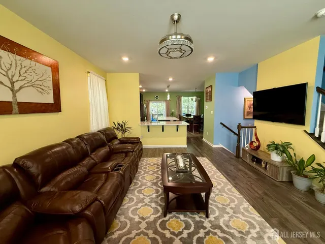 a living room with stainless steel appliances kitchen island granite countertop a refrigerator a sink a dining table and chairs with wooden floor