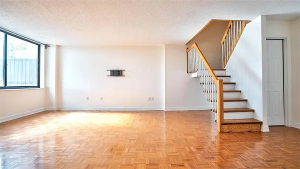 a view of an empty room with wooden floor and stairs