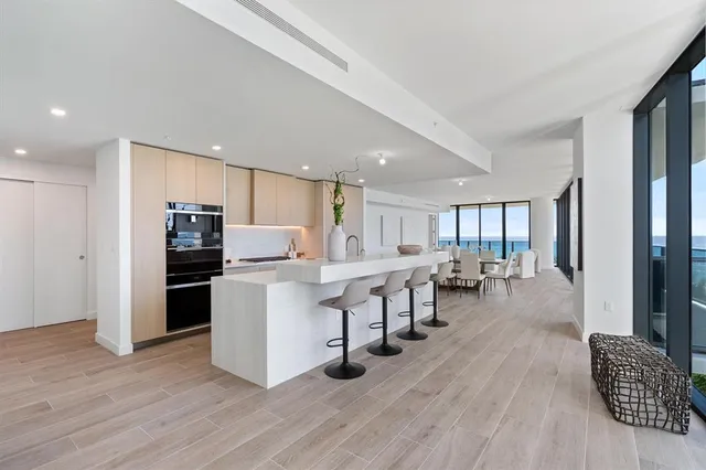 a living room with stainless steel appliances furniture wooden floor and a kitchen view