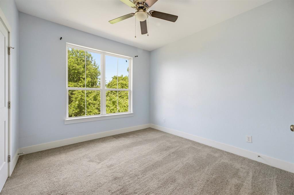 745 North Miller Avenue Stephenville, TX 76401 - Photo 24 of 31 Spacious room featuring a large window with white trim, light blue wall color, gray carpet, white baseboards, and a ceiling fan