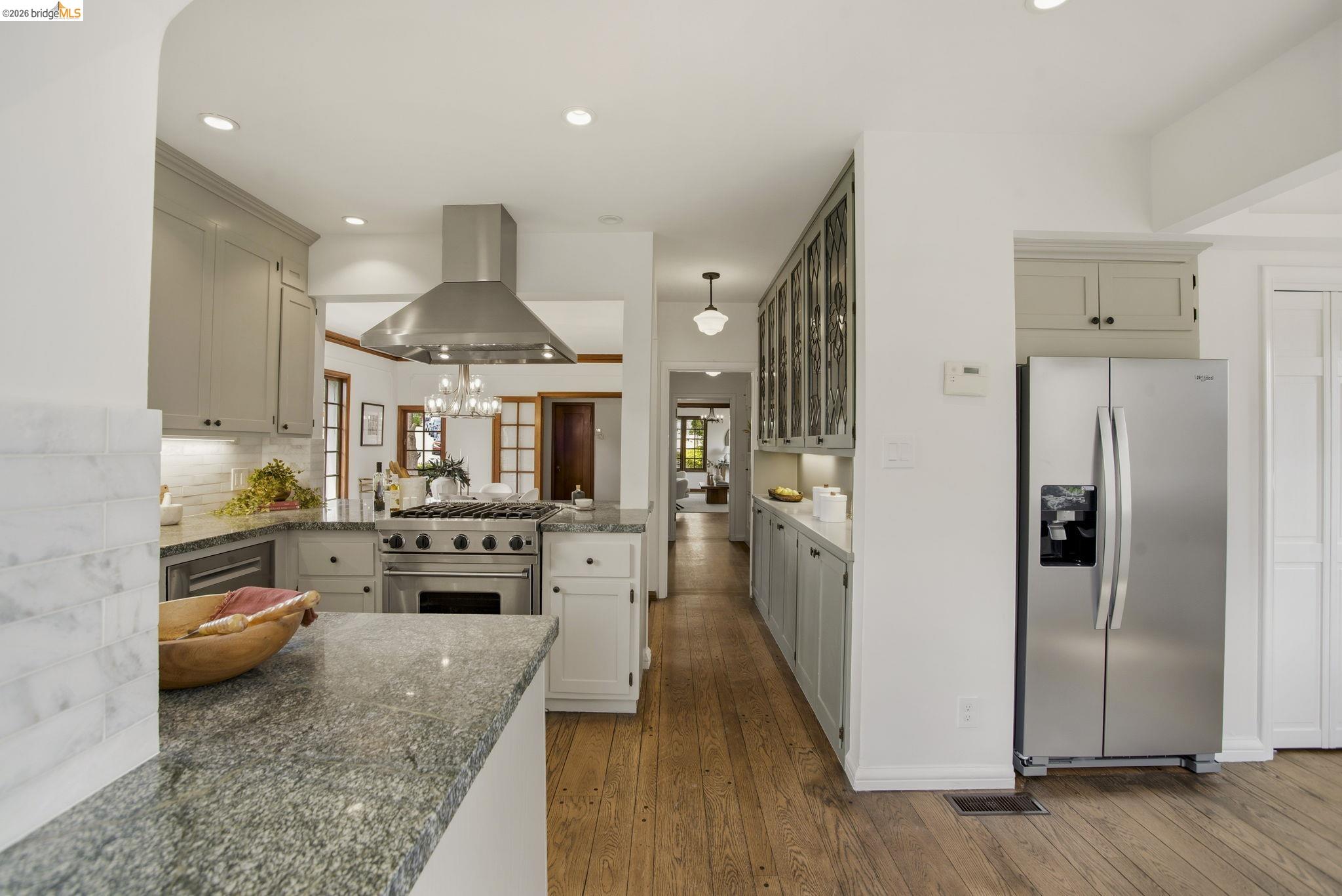 1087 Hubert Road Oakland, CA 94610 - Photo 14 of 67 Gourmet kitchen featuring a professional-grade range, stainless steel vent hood, ample cabinetry with under-cabinet lighting, granite countertops, and wood-finish flooring