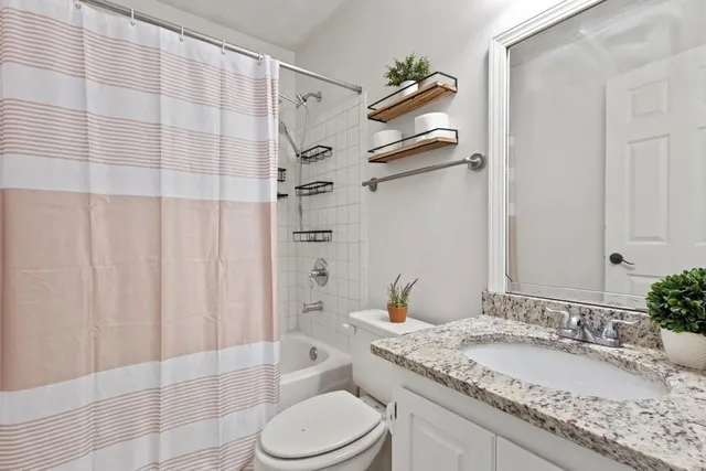 a bathroom with a granite countertop sink toilet a mirror and shower curtain