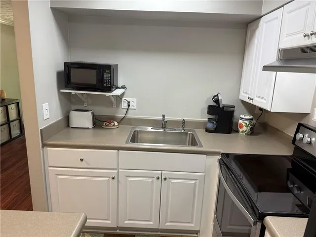 a kitchen with white cabinets a sink and a stove with wooden floor