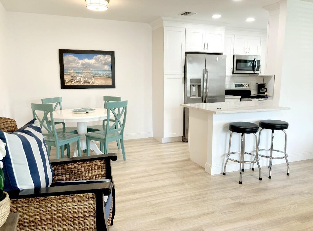 1155 South Drive Circle, Unit A Delray Beach, FL 33445 - Photo 7 of 21 a kitchen with stainless steel appliances kitchen island granite countertop a refrigerator a stove a microwave a dining table and chairs with wooden floor