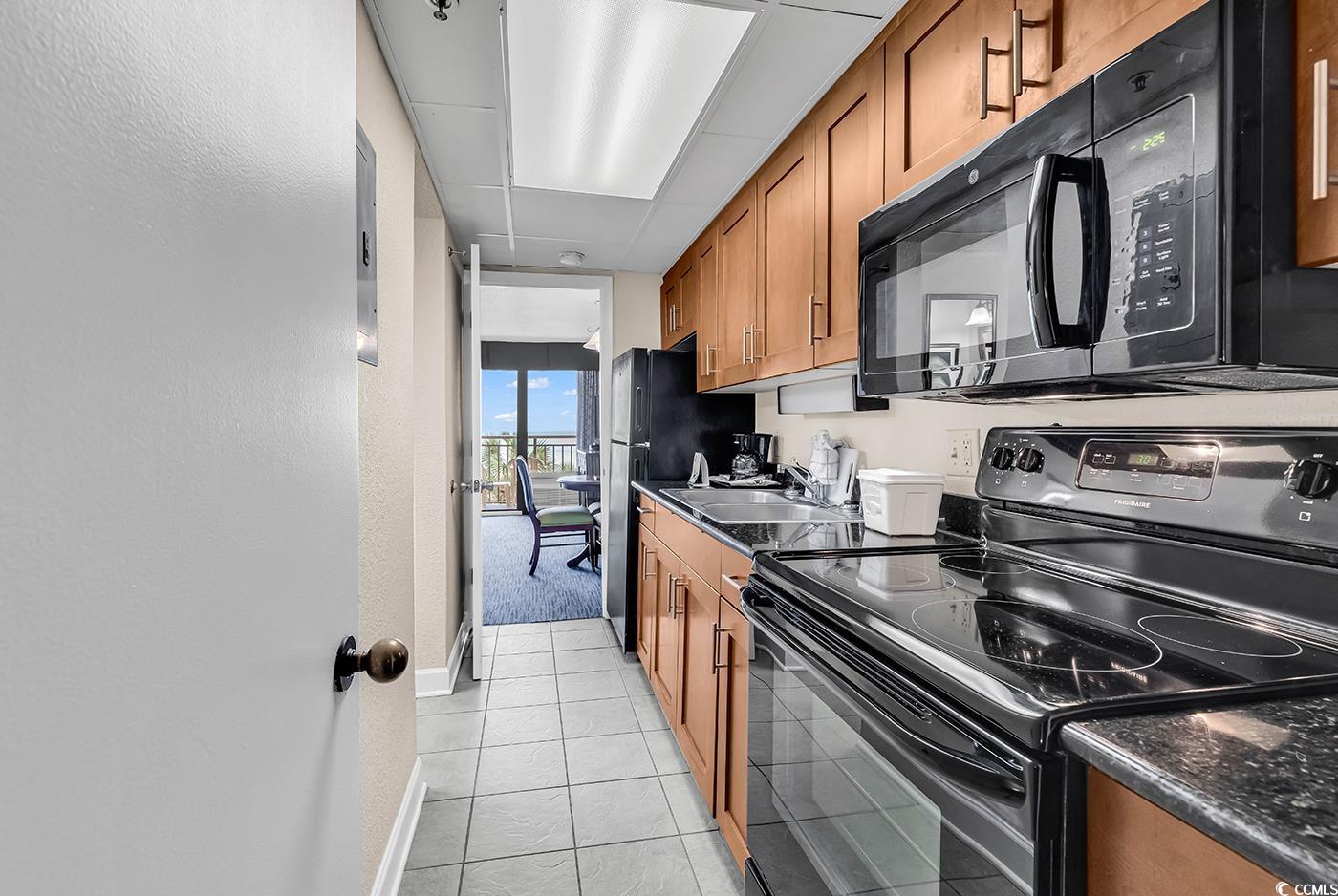 1202 North Ocean Boulevard, Unit 310 Myrtle Beach, SC 29577 - Photo 10 of 29 Kitchen featuring black appliances, brown cabinets, light tile patterned floors, and a textured wall