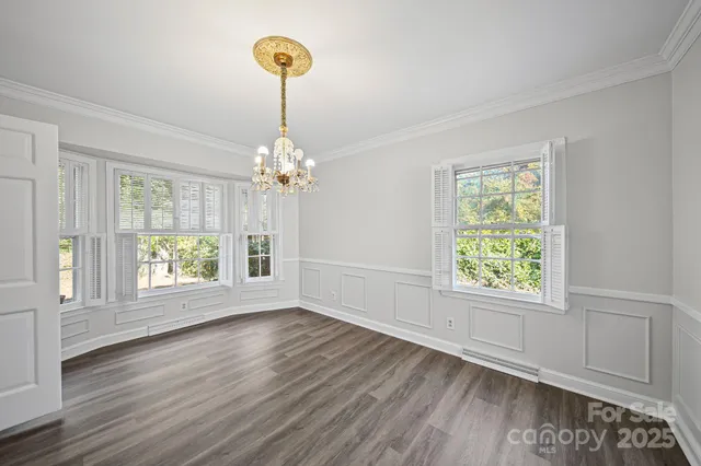 an empty room with wooden floor chandelier and windows