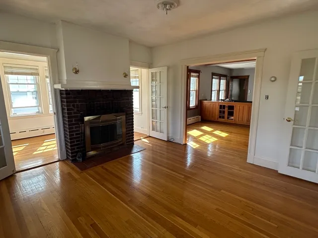 a view of an empty room with wooden floor fireplace and a window