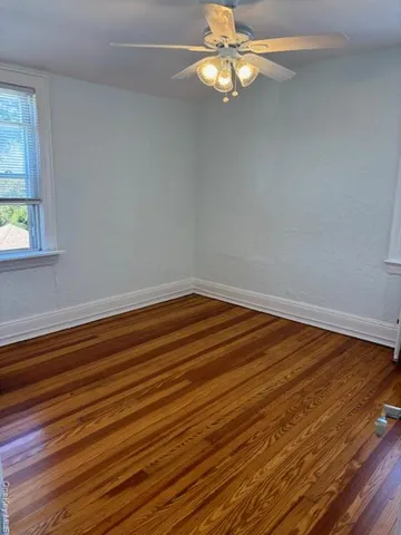 an empty room with wooden floor fan and window