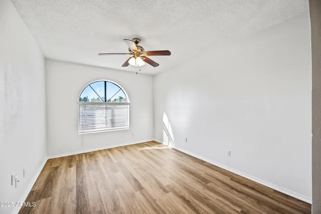 an empty room with wooden floor fan and windows