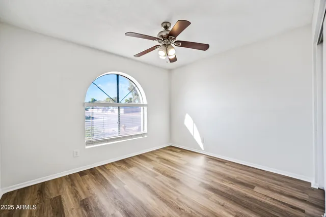 an empty room with wooden floor fan and windows