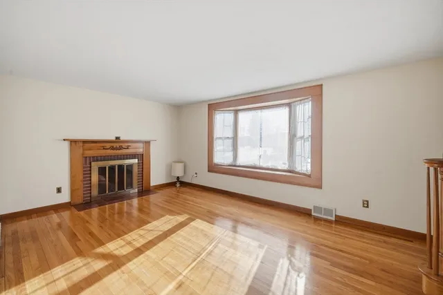a view of an empty room with window and hardwood floor