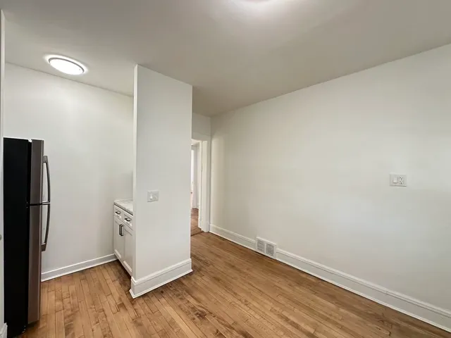an empty room with wooden floor and a refrigerator