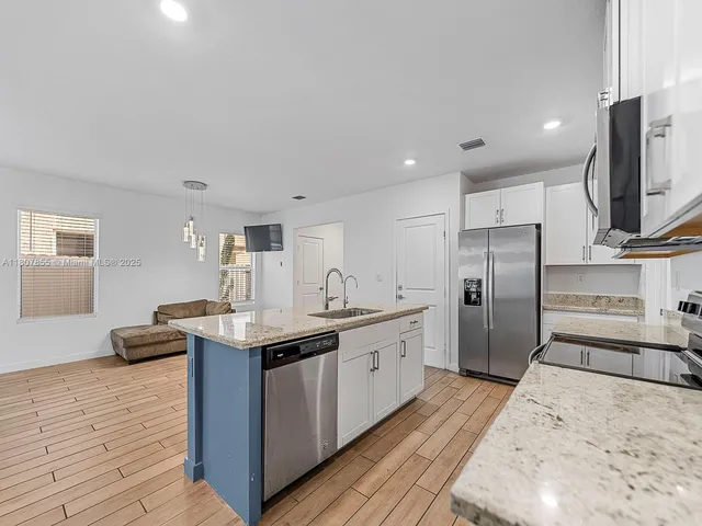 a kitchen with stainless steel appliances kitchen island granite countertop a sink refrigerator and cabinets
