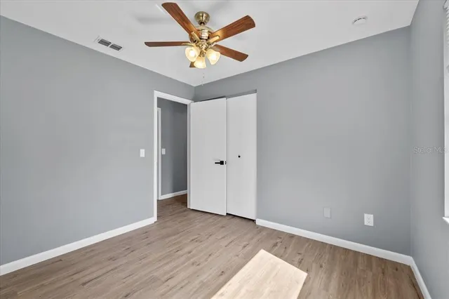 an empty room with wooden floor and a ceiling fan