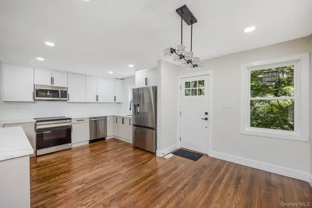 a kitchen with stainless steel appliances granite countertop a refrigerator a sink dishwasher a stove and white countertops with wooden floor