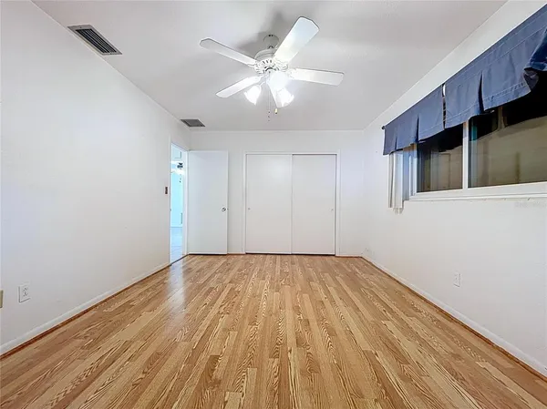 a view of an empty room with wooden floor and a ceiling fan