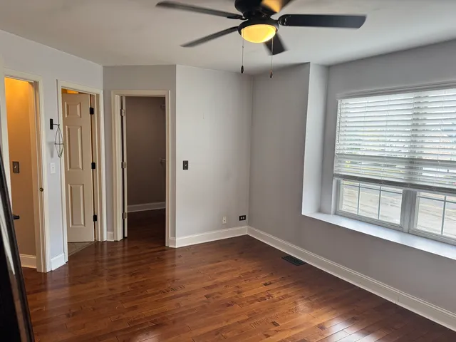 an empty room with wooden floor fan and windows