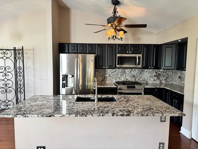 a kitchen with kitchen island granite countertop a stove top oven a sink a counter space and cabinets