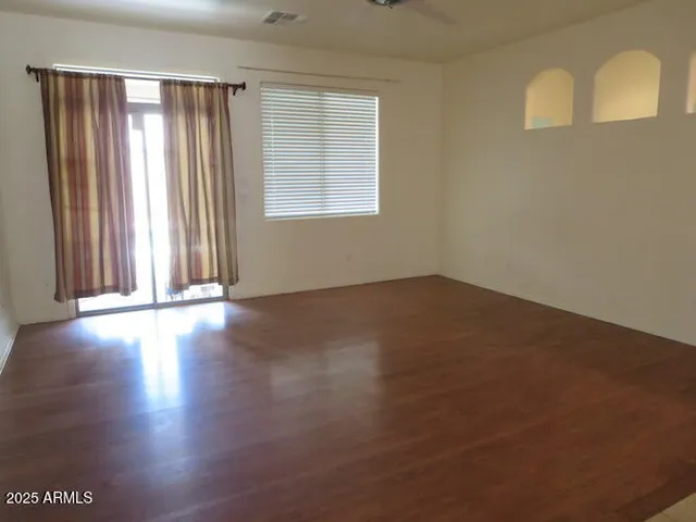 an empty room with wooden floor and windows with curtains