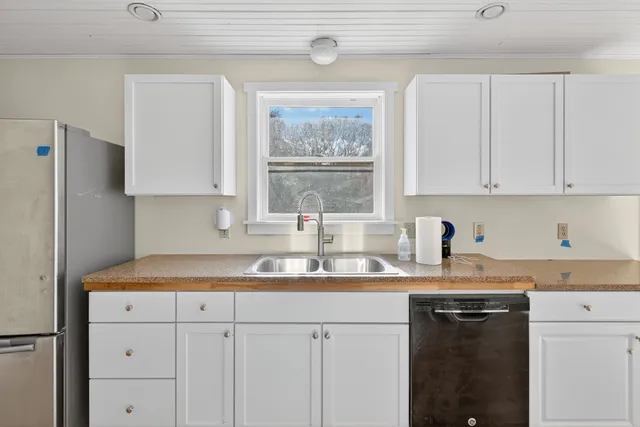 a kitchen with stainless steel appliances granite countertop a sink dishwasher a refrigerator and white cabinets with wooden floor