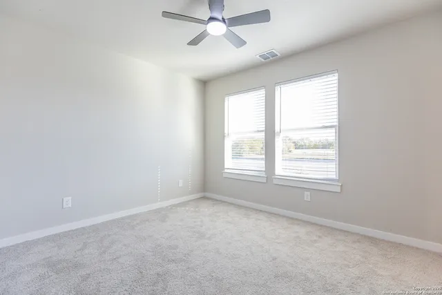 an empty room with chandelier fan and windows