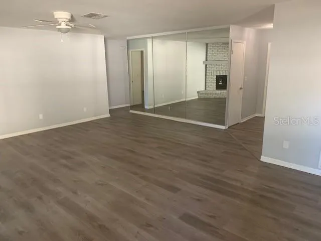 an empty room with wooden floor chandelier fan and windows