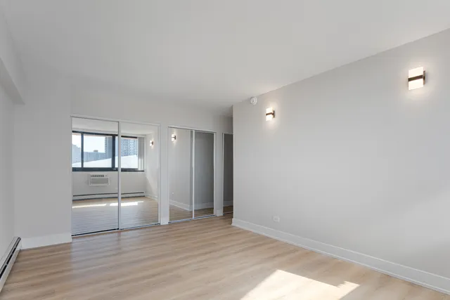 a view of empty room with wooden floor and kitchen