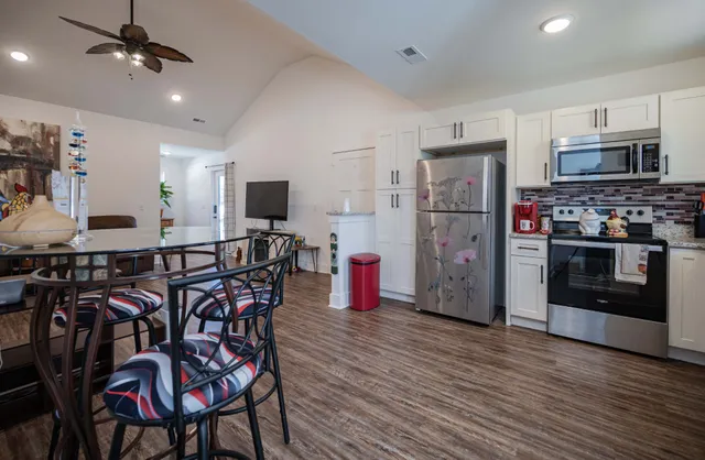 a kitchen with stainless steel appliances kitchen island granite countertop a stove top oven a sink dishwasher a dining table and chairs with wooden floor