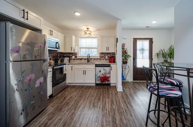 a kitchen with stainless steel appliances granite countertop a refrigerator a stove top oven a sink dishwasher and white cabinets with wooden floor