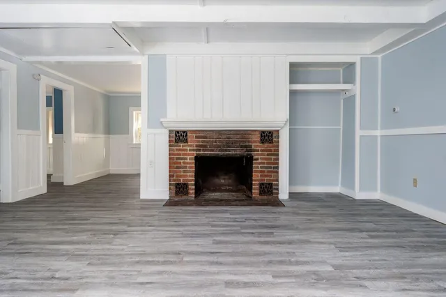 a view of an empty room with wooden floor fireplace and a window