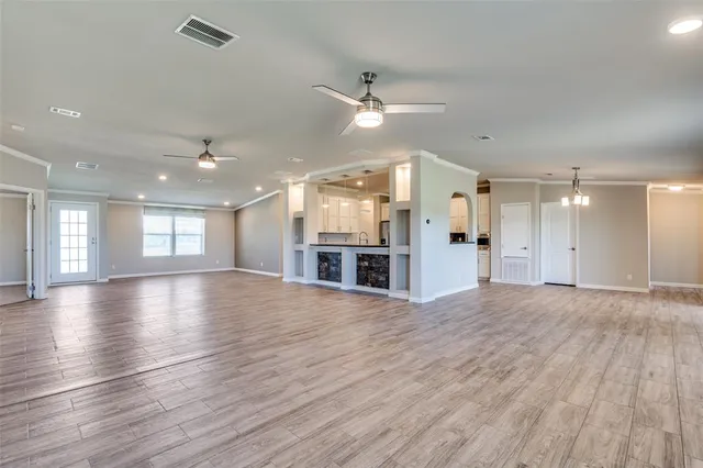 an empty room with wooden floor kitchen view and a window