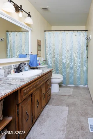 a bathroom with a granite countertop sink a toilet a mirror and shower