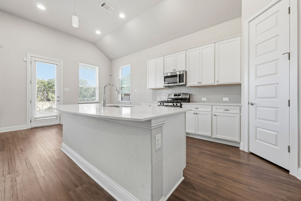 2032 Base Burner Path Leander, TX 78641 - Photo 13 of 34 Kitchen featuring a central island with an integrated sink, white cabinetry, stainless steel appliances, a tiled backsplash, and wood-finish flooring