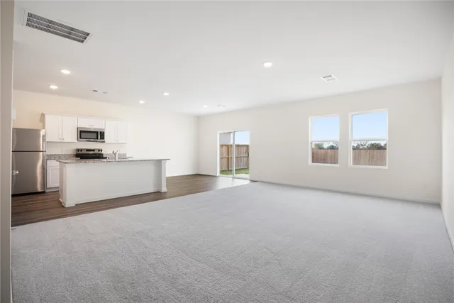a view of an empty room with kitchen and window