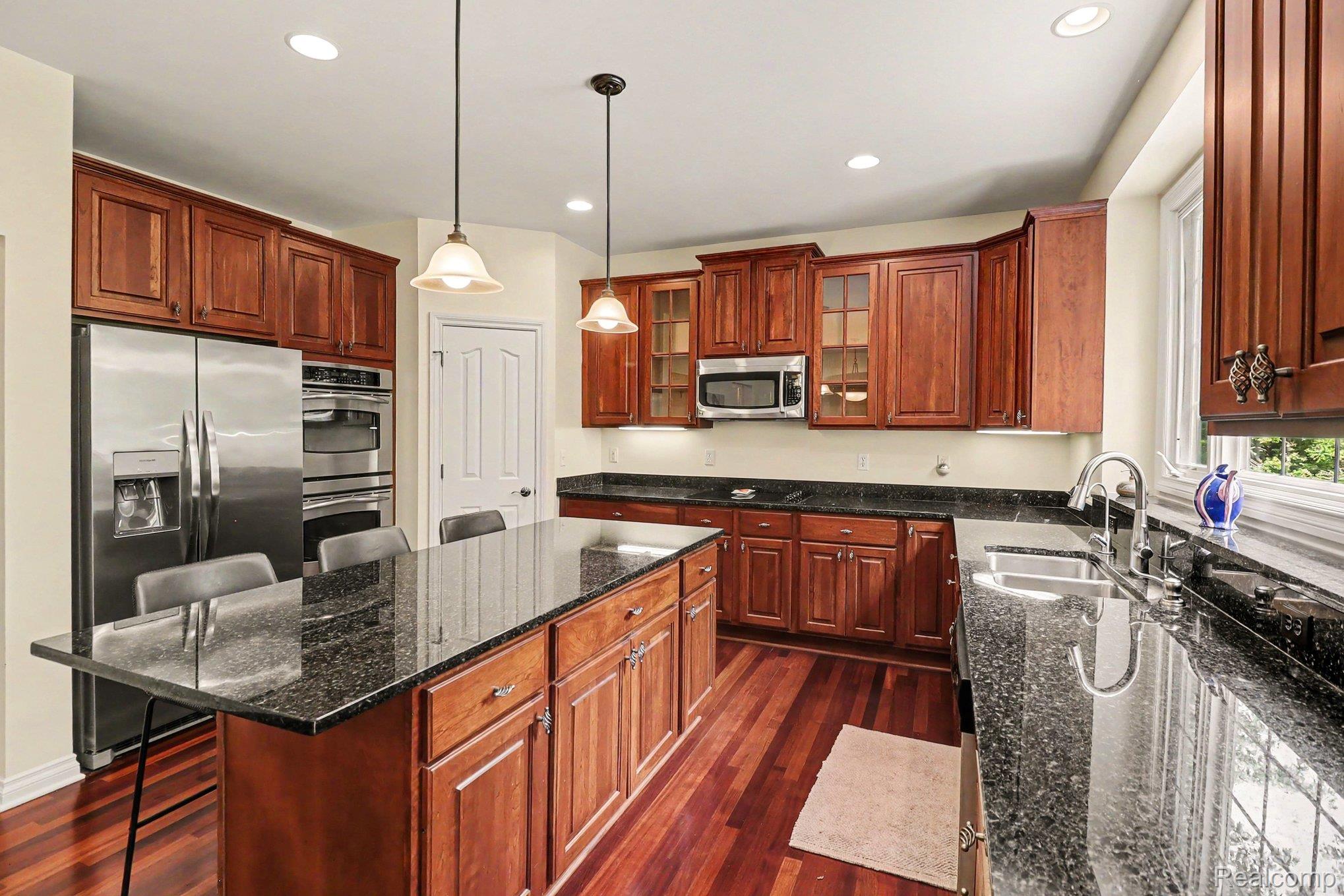 10490 Deer Ridge Trail Holly, MI 48442 - Photo 14 of 56 Kitchen featuring rich wood cabinetry, dark granite countertops, stainless steel appliances, and wood-finish flooring